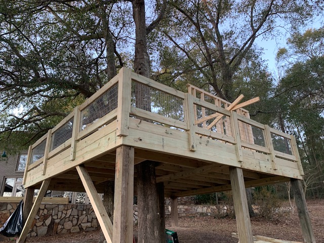 Elevated deck with wire-mesh railing under a large oak tree